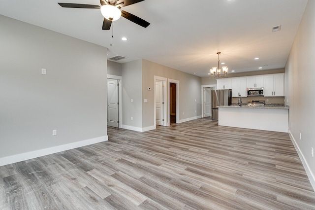 unfurnished living room with sink, ceiling fan with notable chandelier, and light hardwood / wood-style flooring