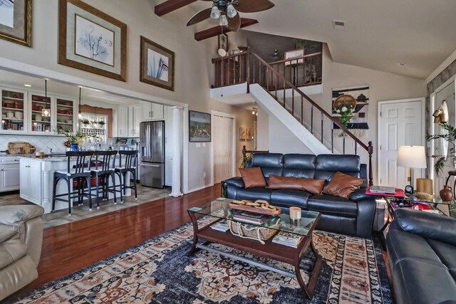 living room featuring stairway, visible vents, dark wood finished floors, a ceiling fan, and high vaulted ceiling