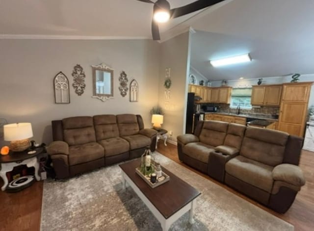 living area with crown molding, light wood-style flooring, baseboards, and vaulted ceiling