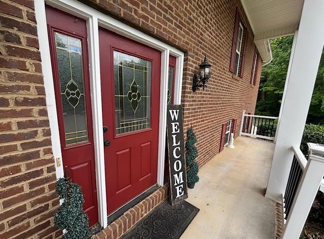 view of exterior entry featuring a porch and brick siding