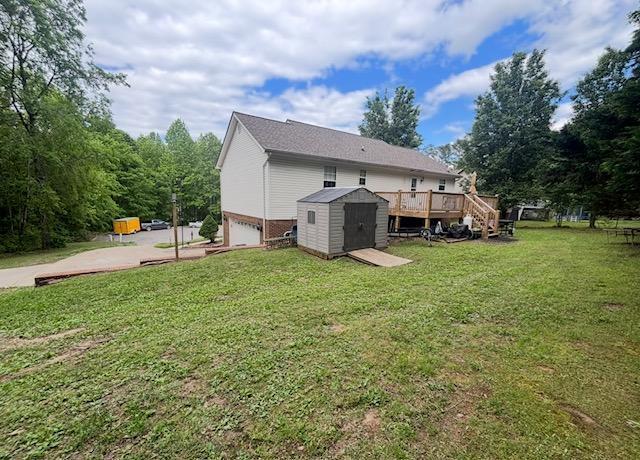rear view of property featuring an outdoor structure, a lawn, a deck, a storage unit, and an attached garage