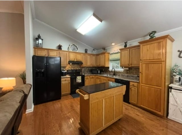 kitchen featuring vaulted ceiling, a sink, black appliances, ornamental molding, and under cabinet range hood