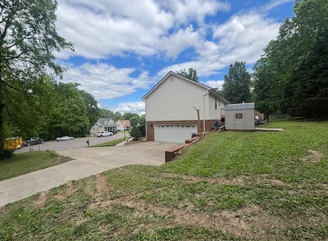 view of home's exterior featuring a garage, brick siding, concrete driveway, a storage shed, and a yard