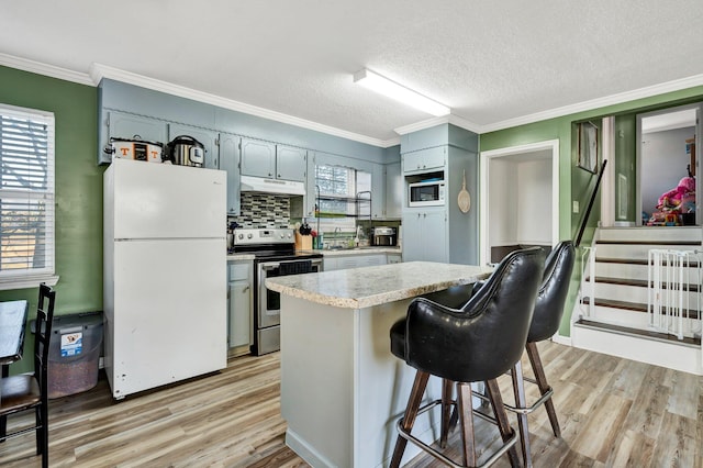 kitchen featuring crown molding, light wood finished floors, light countertops, white appliances, and under cabinet range hood