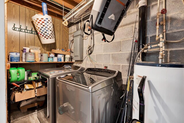 clothes washing area featuring concrete block wall, washing machine and clothes dryer, water heater, laundry area, and electric panel