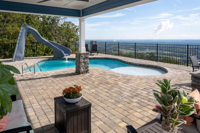 view of swimming pool with a patio, a water view, ceiling fan, and a water slide