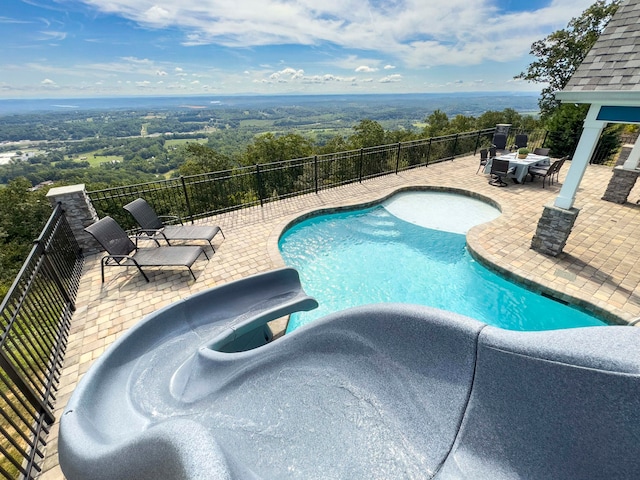 view of pool with a water slide, a patio, and a hot tub