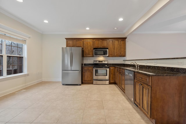 kitchen with sink, crown molding, light tile patterned floors, appliances with stainless steel finishes, and dark stone counters