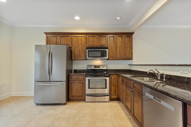 kitchen with sink, crown molding, light tile patterned floors, dark stone countertops, and appliances with stainless steel finishes