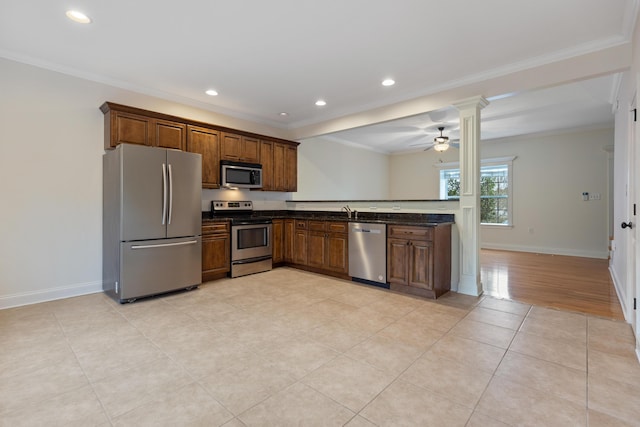 kitchen featuring appliances with stainless steel finishes, sink, dark stone counters, light tile patterned floors, and crown molding