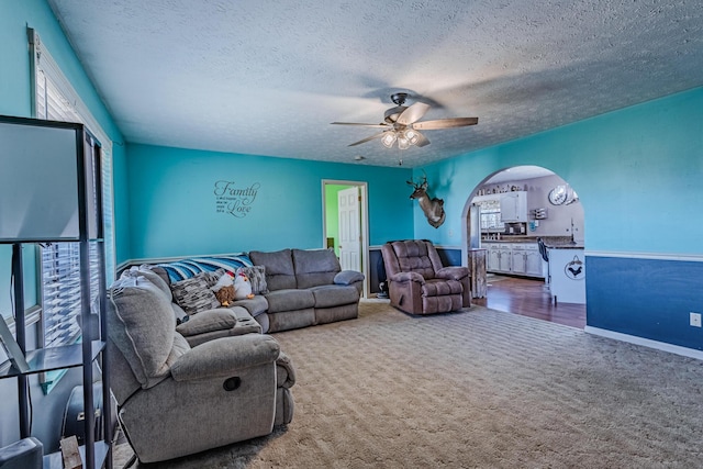 living area with a ceiling fan, carpet, arched walkways, and a textured ceiling