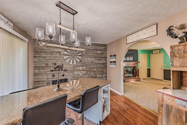 kitchen with arched walkways, a textured ceiling, a brick fireplace, and wood finished floors