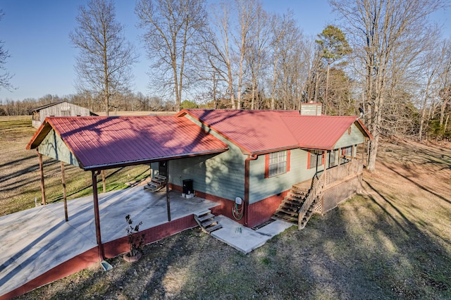 view of front of home featuring stairway, gravel driveway, metal roof, an attached carport, and a chimney