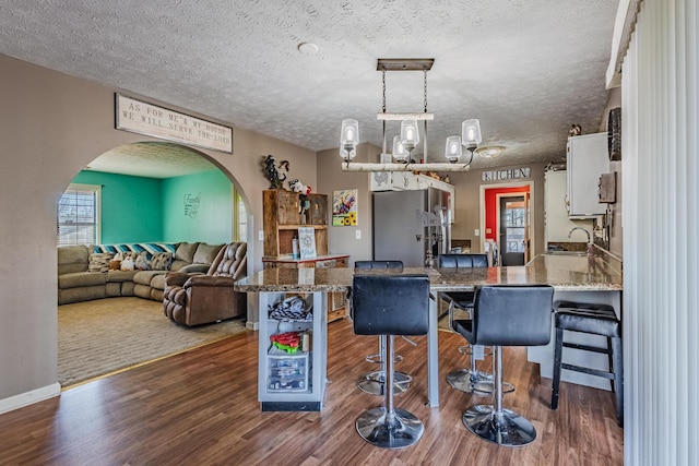 kitchen featuring arched walkways, wood finished floors, stainless steel fridge with ice dispenser, and white cabinetry