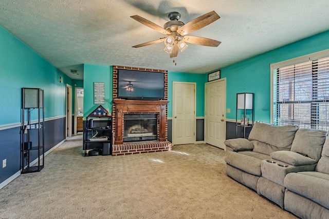 carpeted living area featuring a ceiling fan, a fireplace, wainscoting, and a textured ceiling