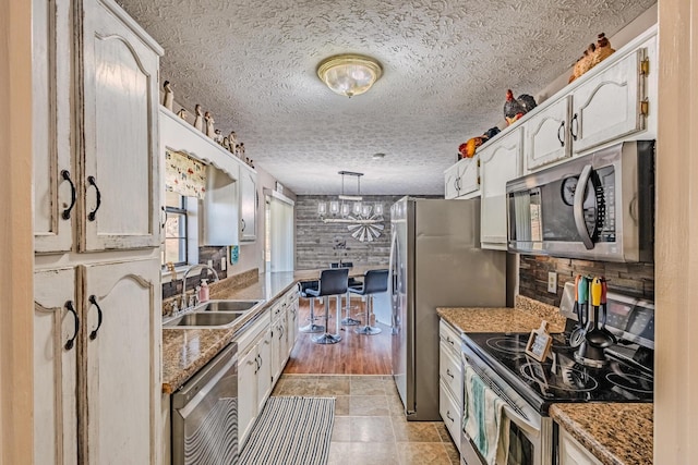 kitchen with white cabinetry, pendant lighting, appliances with stainless steel finishes, a textured ceiling, and a sink