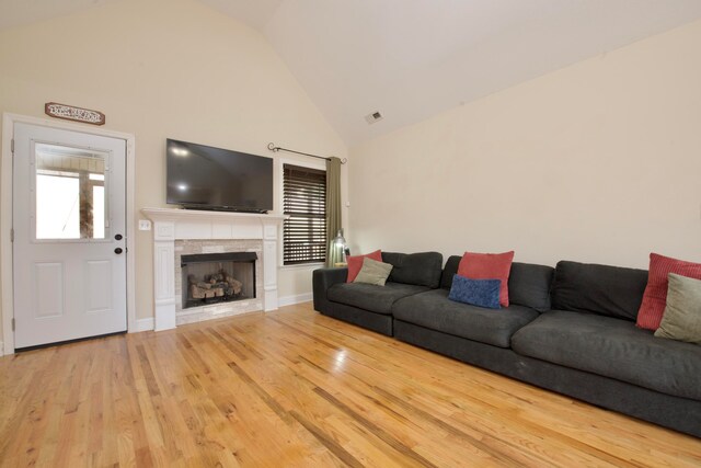 living room with a tiled fireplace, high vaulted ceiling, and light hardwood / wood-style flooring