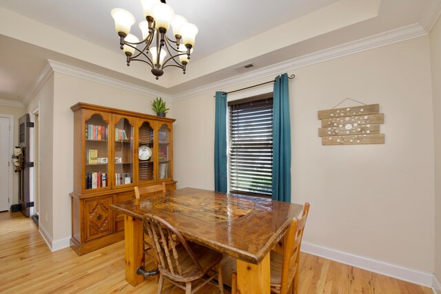 dining room with light wood-type flooring, ornamental molding, a tray ceiling, and an inviting chandelier