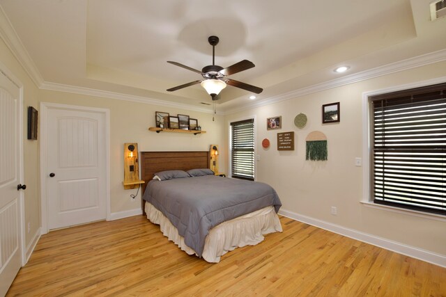 bedroom with light wood-type flooring, a tray ceiling, ceiling fan, and crown molding