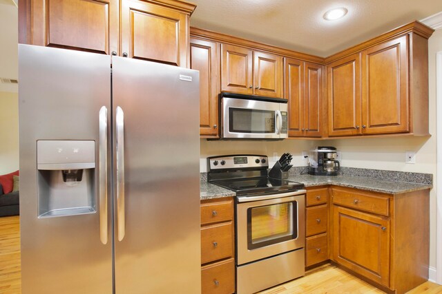 kitchen with dark stone countertops, light hardwood / wood-style floors, and appliances with stainless steel finishes