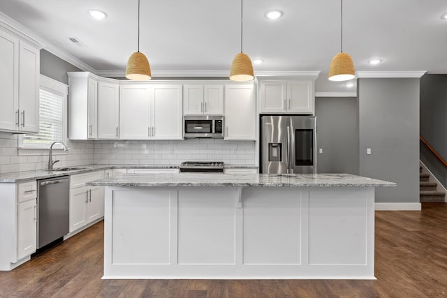 kitchen with light stone countertops, appliances with stainless steel finishes, white cabinets, a kitchen island, and hanging light fixtures