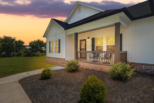 property exterior at dusk with a lawn and covered porch