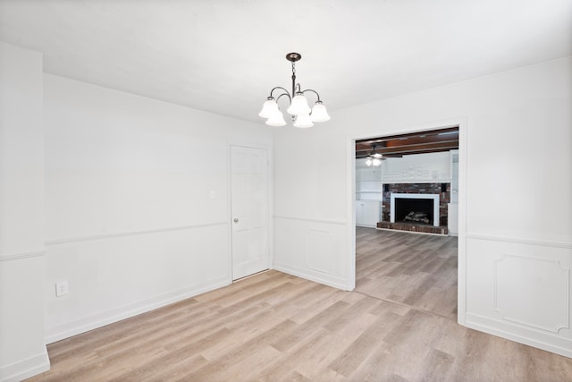 unfurnished dining area featuring a fireplace, light hardwood / wood-style floors, and ceiling fan with notable chandelier