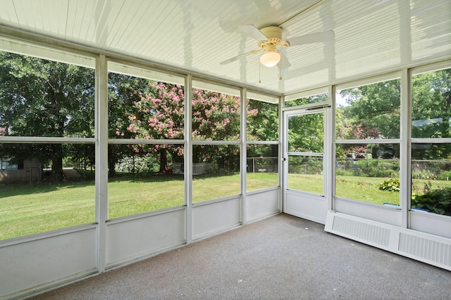 unfurnished sunroom featuring radiator heating unit, plenty of natural light, and ceiling fan