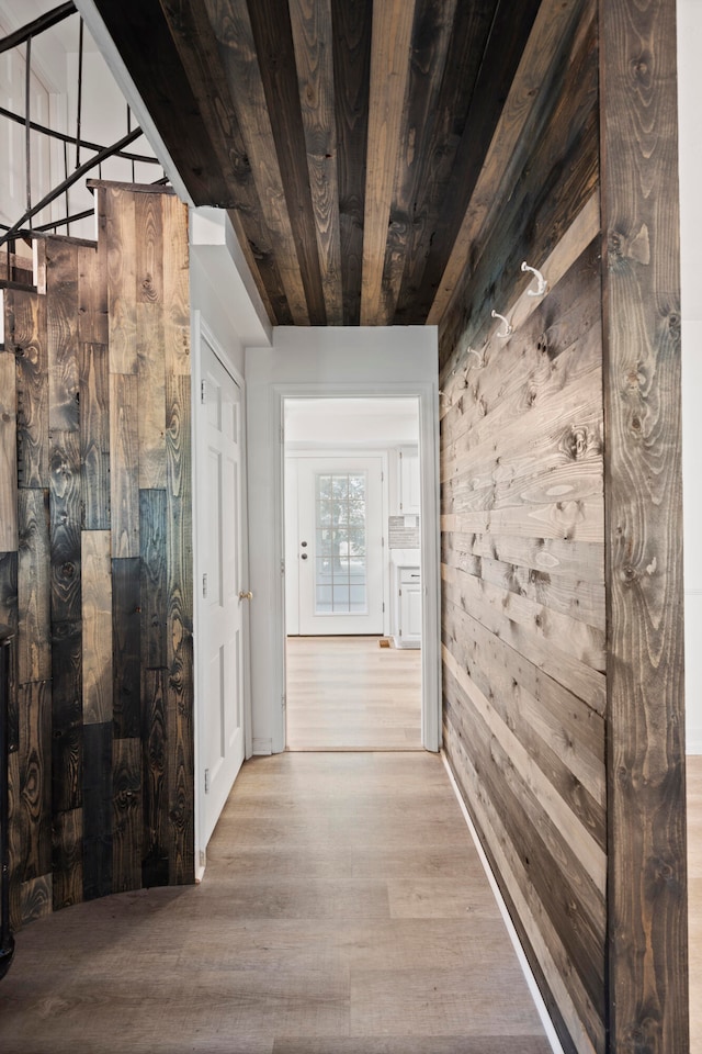 corridor with light wood-type flooring, wooden walls, and wood ceiling