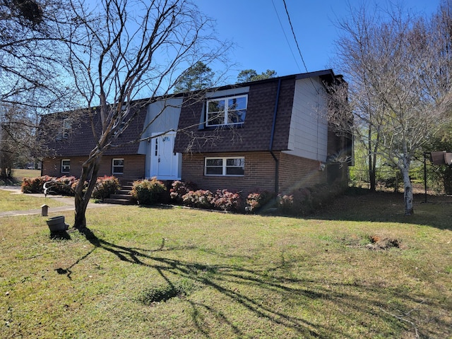 view of front of home featuring a front yard, brick siding, and roof with shingles