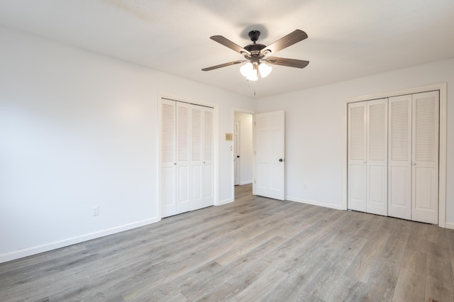 unfurnished bedroom featuring multiple closets, ceiling fan, and light hardwood / wood-style flooring