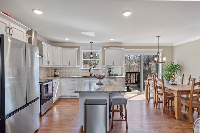 kitchen featuring a center island, decorative light fixtures, light stone countertops, appliances with stainless steel finishes, and white cabinets