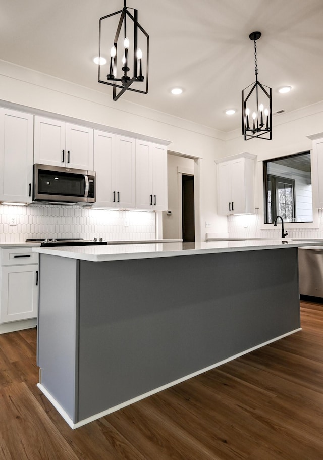 kitchen with pendant lighting, appliances with stainless steel finishes, an inviting chandelier, white cabinets, and a kitchen island