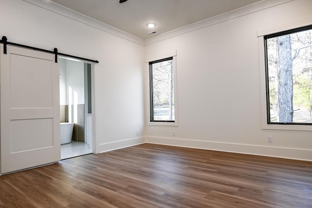 unfurnished bedroom featuring ornamental molding, a barn door, and dark hardwood / wood-style floors