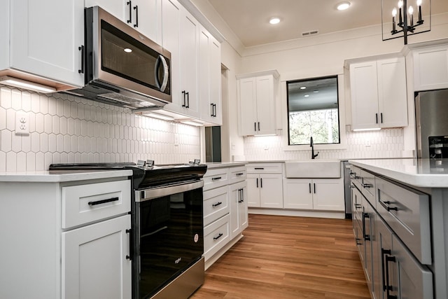 kitchen with sink, white cabinetry, decorative light fixtures, light wood-type flooring, and appliances with stainless steel finishes