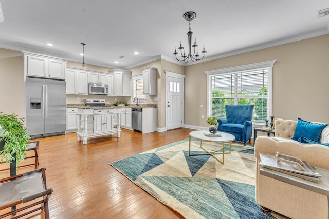 living room with crown molding, light hardwood / wood-style flooring, a chandelier, and sink