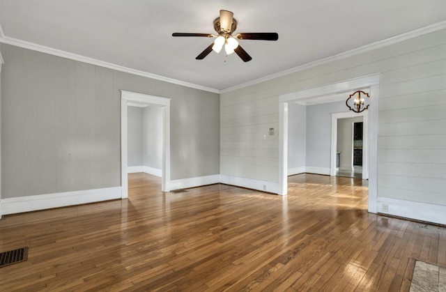 spare room featuring ceiling fan with notable chandelier, wood-type flooring, baseboards, ornamental molding, and visible vents