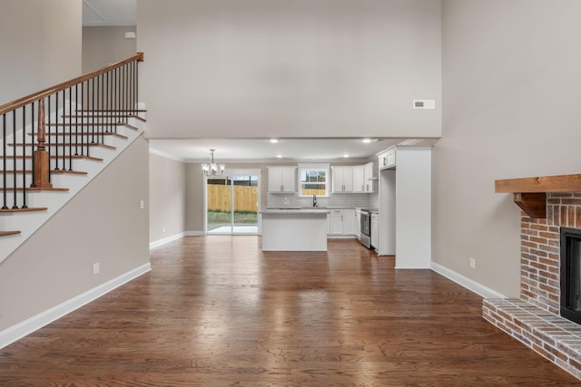 unfurnished living room with an inviting chandelier, dark hardwood / wood-style flooring, sink, and a brick fireplace