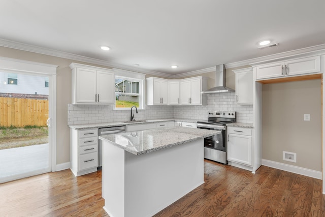 kitchen with sink, wall chimney range hood, a kitchen island, stainless steel range with electric cooktop, and white cabinets