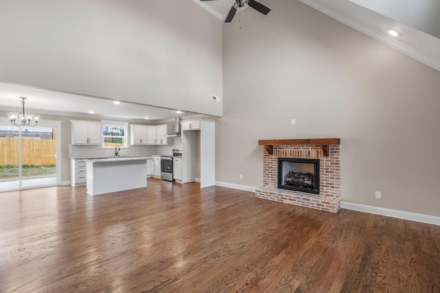 unfurnished living room featuring sink, dark wood-type flooring, ceiling fan with notable chandelier, and a brick fireplace