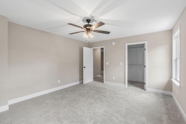 unfurnished bedroom featuring a walk in closet, a closet, ceiling fan, and light colored carpet