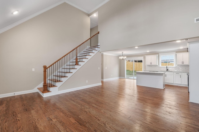 unfurnished living room featuring hardwood / wood-style flooring, a notable chandelier, ornamental molding, and sink