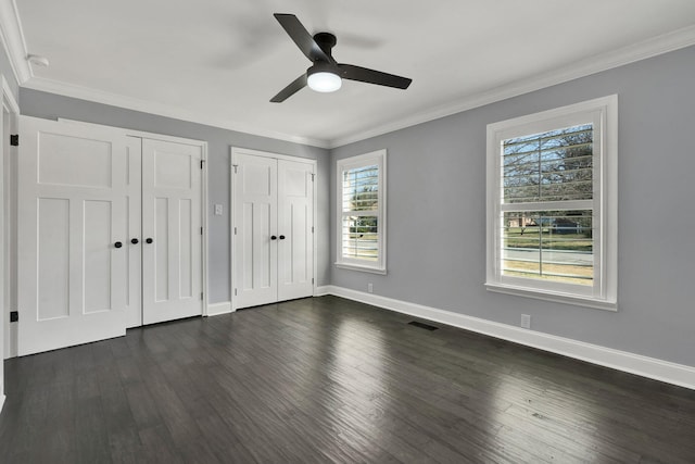 unfurnished bedroom with dark wood-style floors, ornamental molding, two closets, and baseboards