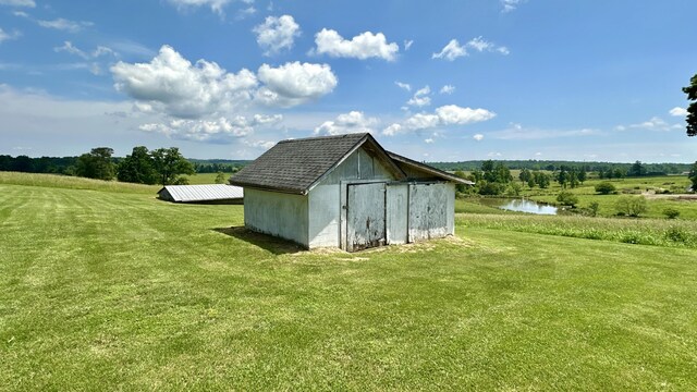 view of outdoor structure with a rural view, a water view, and a yard