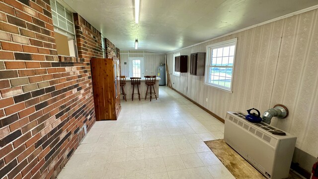 corridor featuring ornamental molding, brick wall, vaulted ceiling, water heater, and radiator heating unit