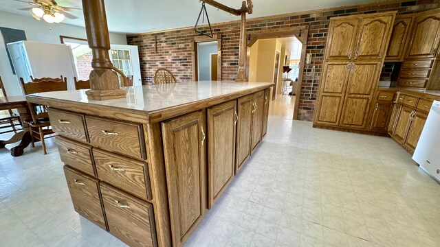 kitchen with white dishwasher, a kitchen island, ceiling fan, and brick wall