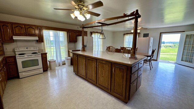 kitchen featuring white appliances, a center island, ceiling fan, and a healthy amount of sunlight