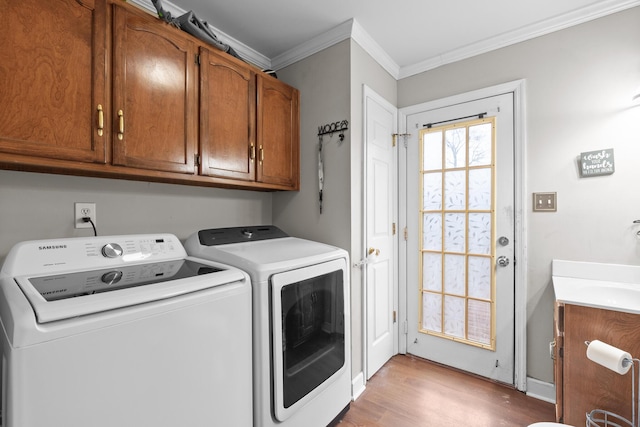 laundry room featuring cabinets, washing machine and clothes dryer, ornamental molding, and light hardwood / wood-style flooring