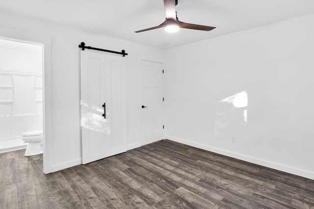 spare room with a barn door, ceiling fan, and dark wood-type flooring