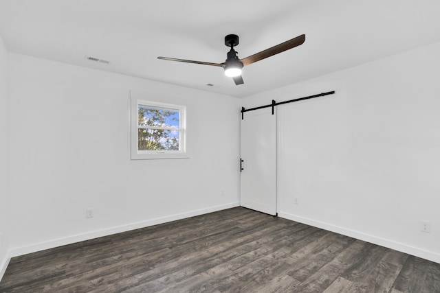 empty room with a barn door, ceiling fan, and dark wood-type flooring